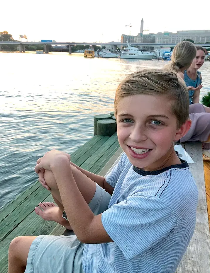 Mitchell sits by a waterfront at sunset, boats and a city skyline are visible.